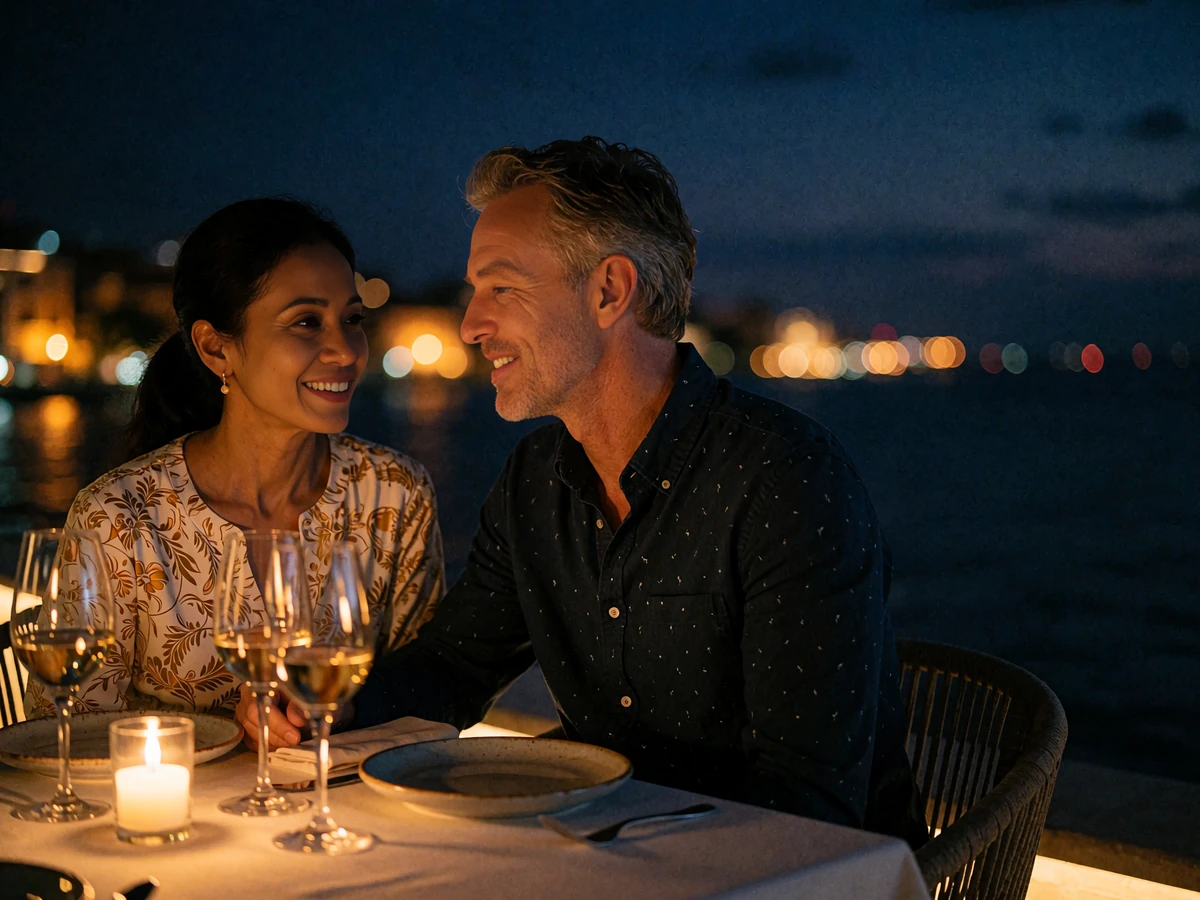 Couple leaning toward each other in conversation at a candlelit dinner table on a restaurant terrace overlooking the water